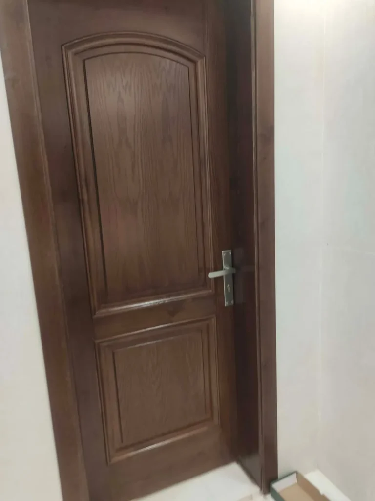 باب خشب داكن بحشوتين مقوّستين بعد التركيب